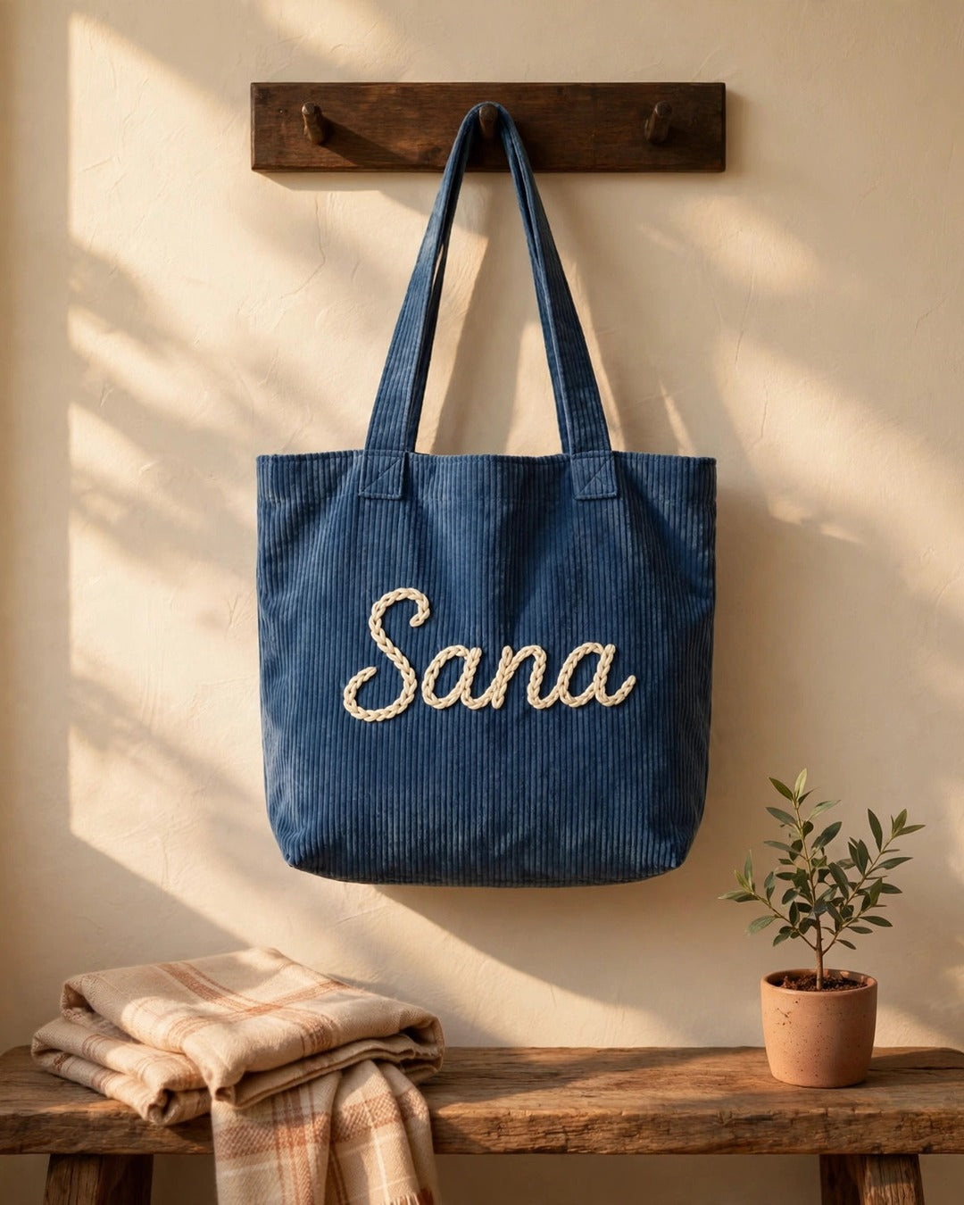 Denim blue corduroy tote bag with the name Sana hand-embroidered, hanging on a wall hook