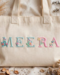 Natural canvas tote with MEERA in pastel floral embroidered alphabet letters