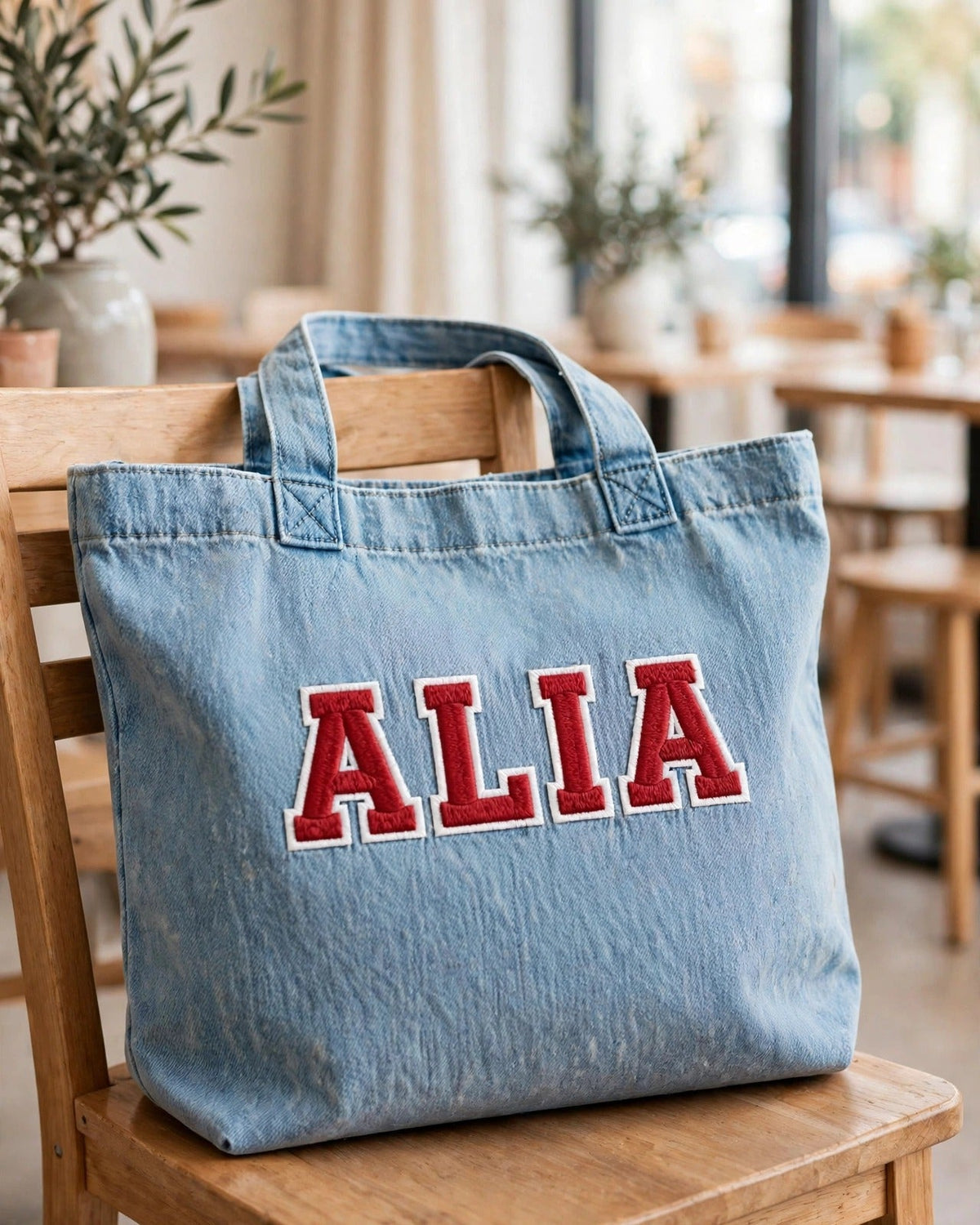 Light denim tote with small red patch letters – lifestyle shot in bright cafe setting