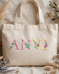 Beige canvas tote with ANVI in pastel floral embroidered alphabet letters