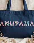 Dark denim canvas tote with ANUPAMA in pastel floral embroidered alphabet letters
