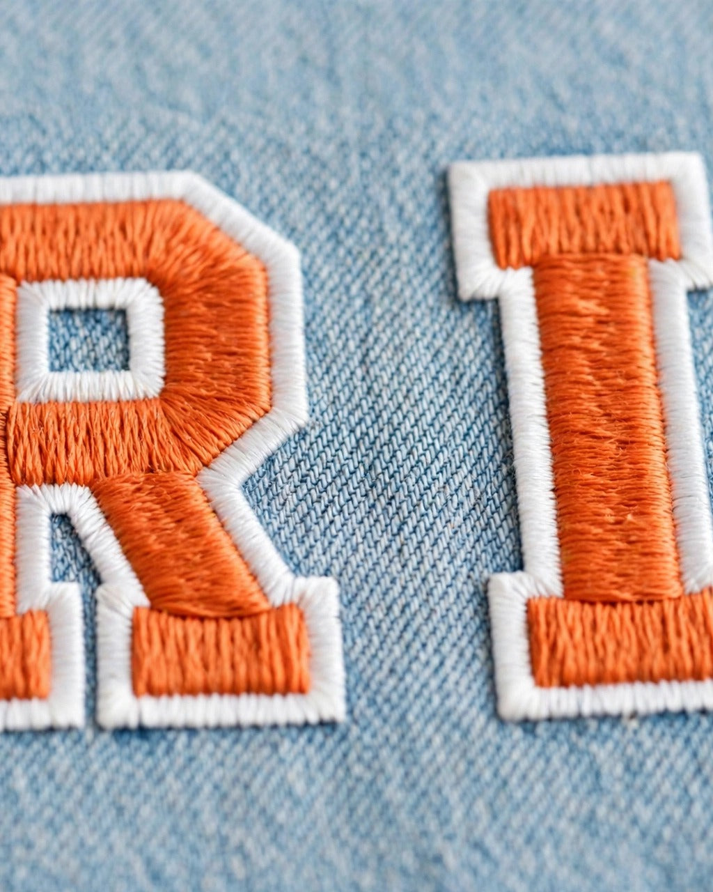 Light denim tote with small orange patch letters – embroidery close-up