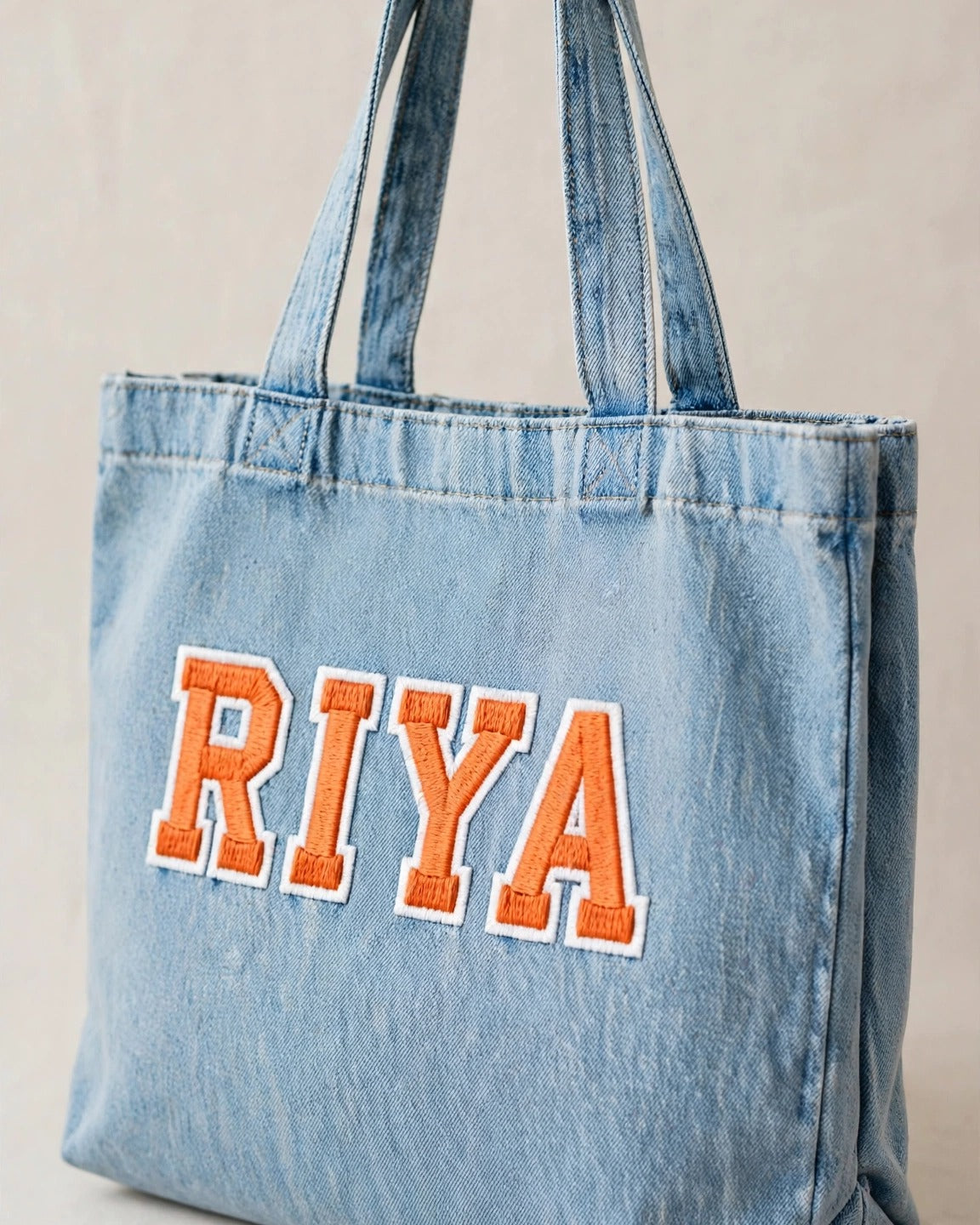 Light denim tote with small orange patch letters – side angle view