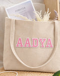 Beige corduroy tote with AADYA in pink embroidered varsity patch letters