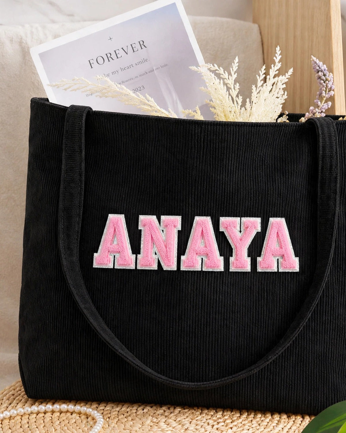 Black corduroy tote with ANAYA in light pink embroidered varsity patch letters