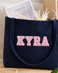 Navy blue corduroy tote with KYRA in light pink embroidered varsity patch letters