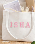 White corduroy tote with ISHA in light pink embroidered varsity patch letters