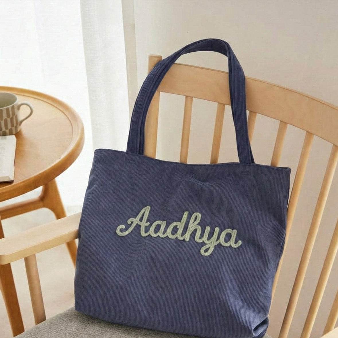 Blue tote bag with 'Aadhya' embroidery on a chair in a room setting